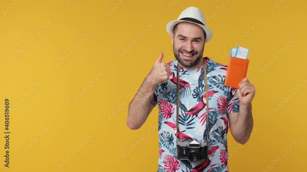 Excited traveler tourist young man in hat isolated on yellow background. Passenger travel on weekends. Air flight journey concept. Hold passport tickets pointing index finger aside showing thumb up Excited traveler tourist young man in hat isolated on yellow background. Passenger travel on weekends. Air flight journey concept. Hold passport tickets pointing index finger aside showing thumb up