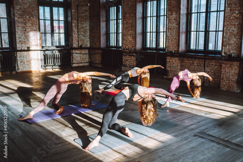 Group of young women wearing sporst wear do complex of stretching yoga asanas in big loft style class at sunny day.