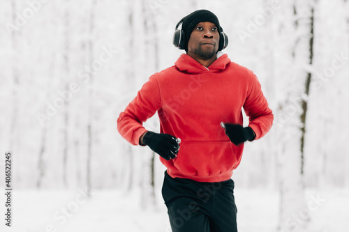 Fototapeta Naklejka Na Ścianę i Meble -  Young african american man running on winter day in forest