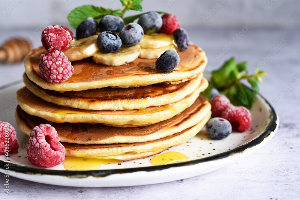 Homemade pancakes with banana, raspberries, blueberries and honey on a light kitchen background. Homemade pancakes with banana, raspberries, blueberries and honey on a light kitchen background.