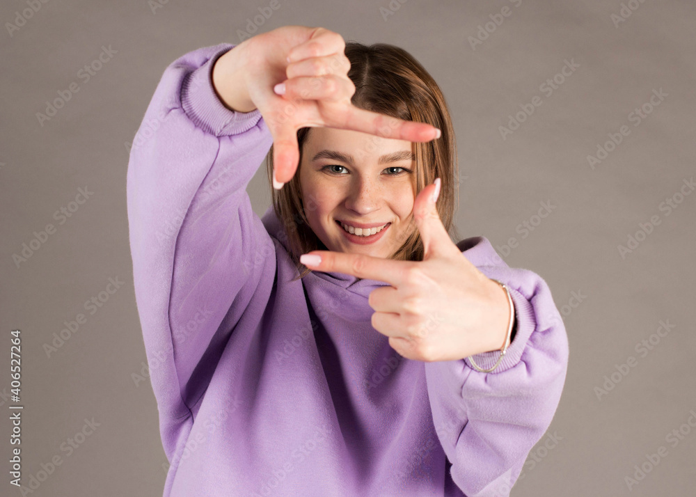 Happy young woman making frame gesture with fingers over gray background Happy young woman making frame gesture with fingers over gray background
