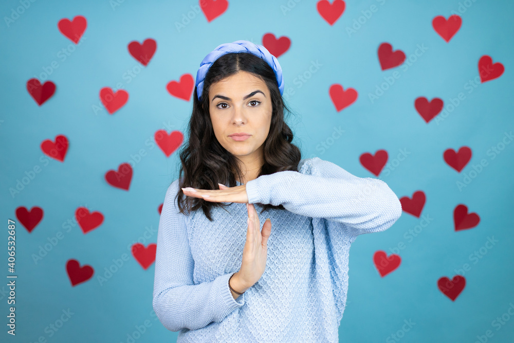 Young beautiful woman over blue background with red hearts Doing time out gesture with hands, frustrated and serious face Young beautiful woman over blue background with red hearts Doing time out gesture with hands, frustrated and serious face