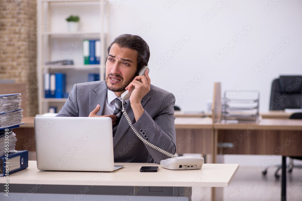 Young male employee unhappy with excessive work in the office Young male employee unhappy with excessive work in the office