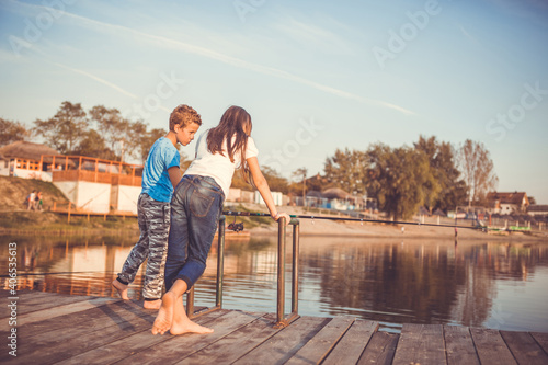 Two young little best friends  boy and girl fishing on a lake in a sunny summer day