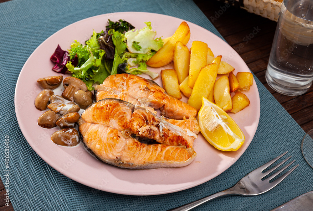 Plate of roasted red fish steaks served with greens, potato, mushrooms and slice of lemon