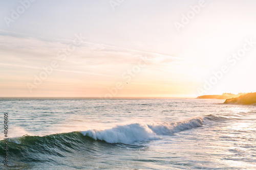 Golden hour sunset with Pacific ocean waves crashing along cliff shoreline of Santa Cruz Bay on California coast