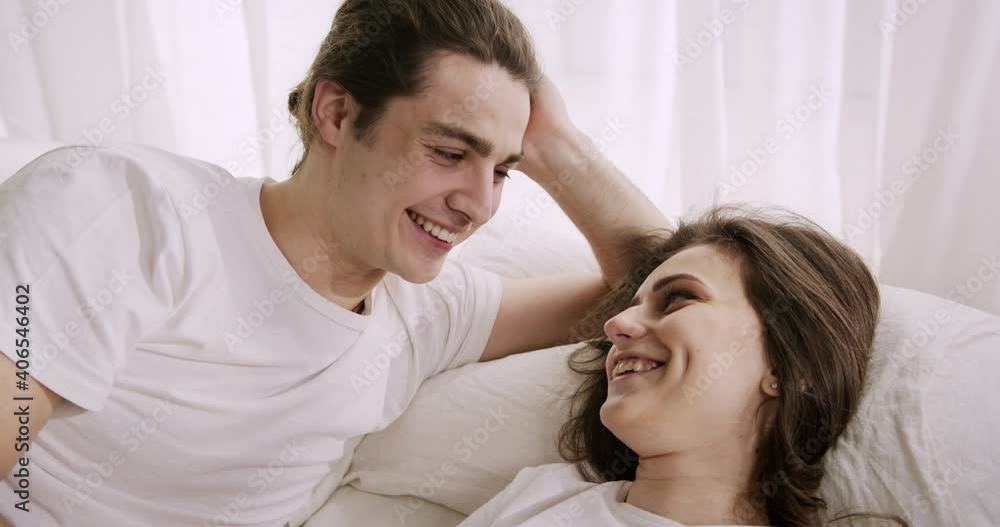 Young romantic couple lying awake in bed, enjoying time together, talking, looking with love, feeling happy. Close-up view. Young romantic couple lying awake in bed, enjoying time together, talking, looking with love, feeling happy. Close-up view.