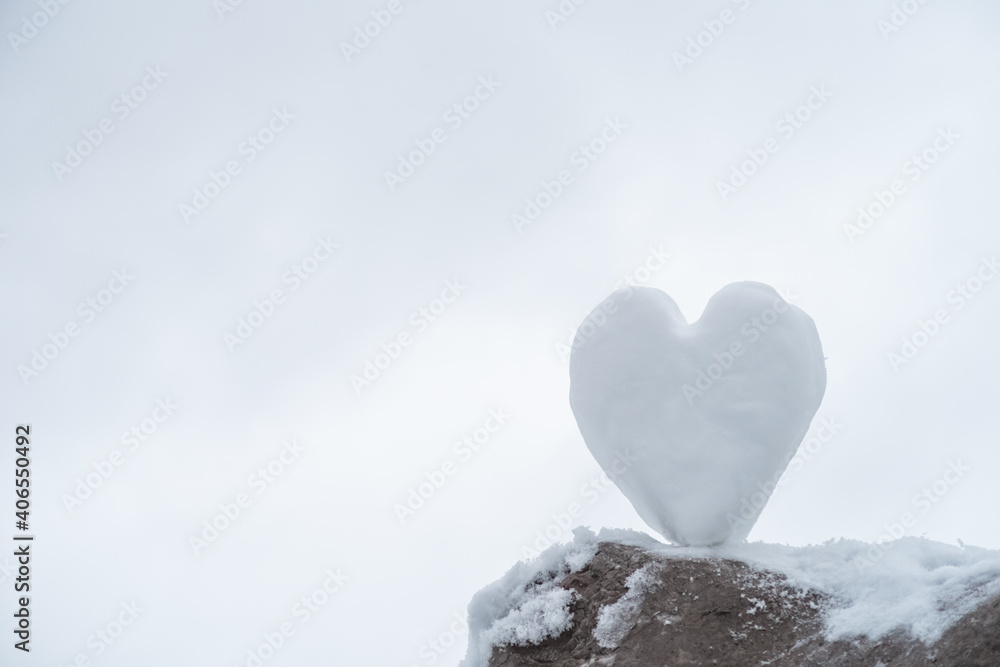 Fototapeta premium Heart shaped snowball standing on a stone with a snowy background