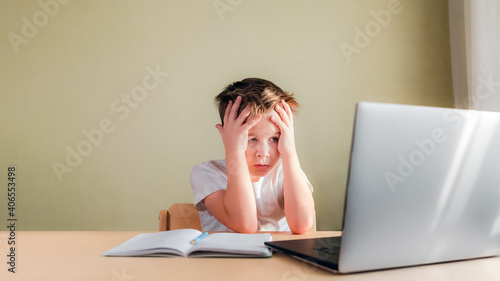 Desperate Child sits at a desk, looks sadly at the computer and holds his head with his hands. Online learning problem concept