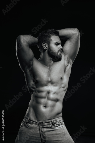 Male fitness model Konstantin Kamynin posing shirtless on black background with hands up