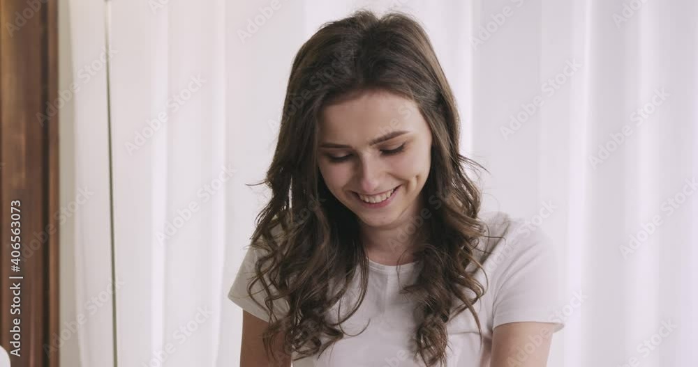 Joyful young woman staying in bed with laptop, socializing online through video call, chatting, greeting a caller. Coronavirus pandemic. Lockdown. Joyful young woman staying in bed with laptop, socializing online through video call, chatting, greeting a caller. Coronavirus pandemic. Lockdown.