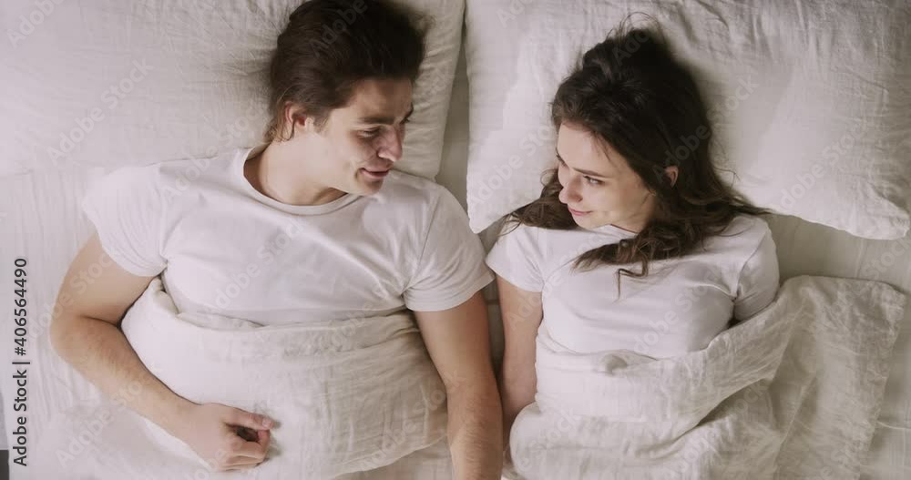 Young Caucasian family couple lying awake together in bed, enjoying pleasant conversation, sharing smiles, feeling happy and relaxed. Comfort home. Young Caucasian family couple lying awake together in bed, enjoying pleasant conversation, sharing smiles, feeling happy and relaxed. Comfort home.