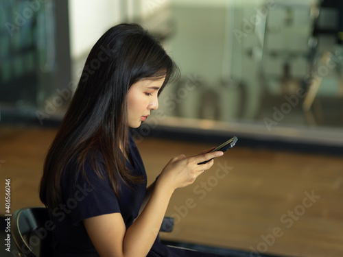 Businesswoman working with smartphone while sitting in glass partition office room
