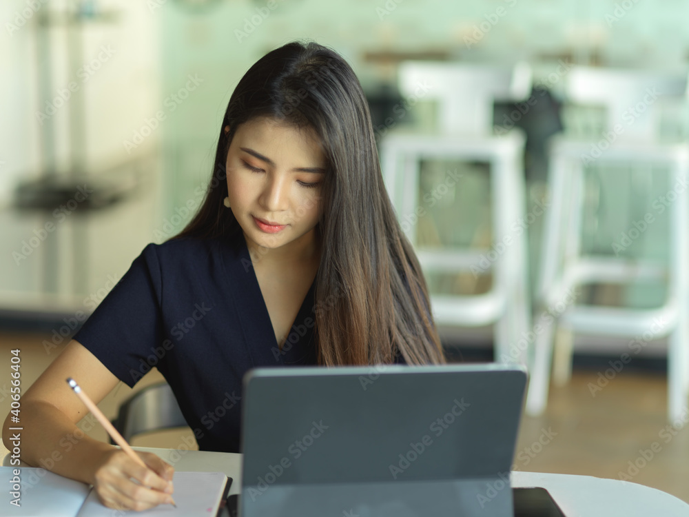 Businesswoman hand writing on notebook while working with laptop on the table Businesswoman hand writing on notebook while working with laptop on the table