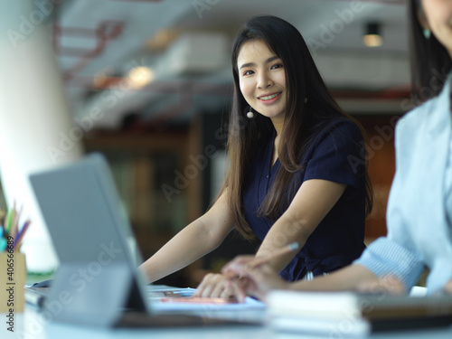 Businesswoman smiling to camera while working with her coworker in office room
