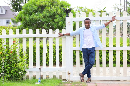 Healthy African American man leaning on the white picket fence in relaxation around the neighborhood with good green environment surrounding with copy space