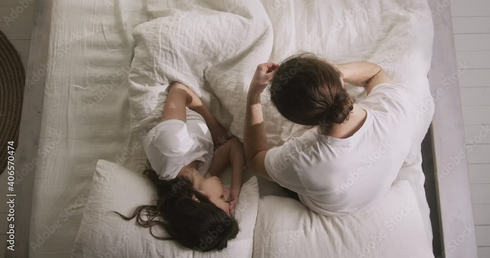 Young family couple staying together in bed. Woman feeling bad, rubbing head, suffering from fever. Worried man checking wife's temperature, calling a doctor. Coronavirus pandemic. Young family couple staying together in bed. Woman feeling bad, rubbing head, suffering from fever. Worried man checking wife's temperature, calling a doctor. Coronavirus pandemic.