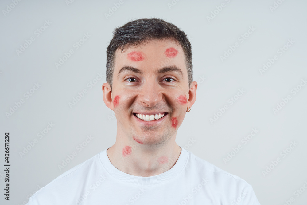 Obraz premium Cheerful man covered with lipstick prints. Studio shot over gray background. Happy Valentine's Day.