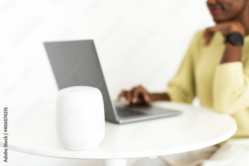 Smart speaker next to laptop with a woman Smart speaker next to laptop with a woman