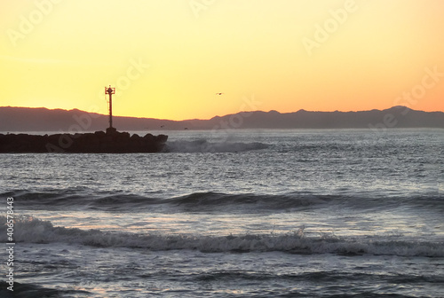 Orange Sunset over ocean with rocky breakwater and beacon forming a channel for boats and ships