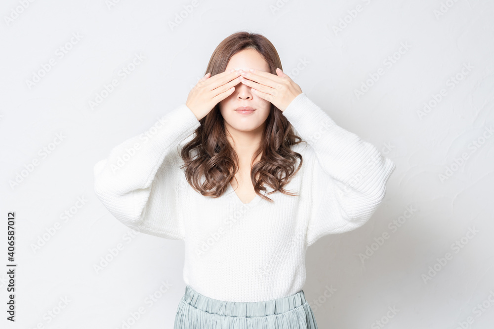 白い壁の前に立って、手で目を隠す若い女性