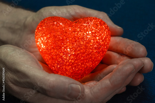 Red glowing heart in male hands on a dark blue background. Valentine's Day concept. Close-up. Copy space.