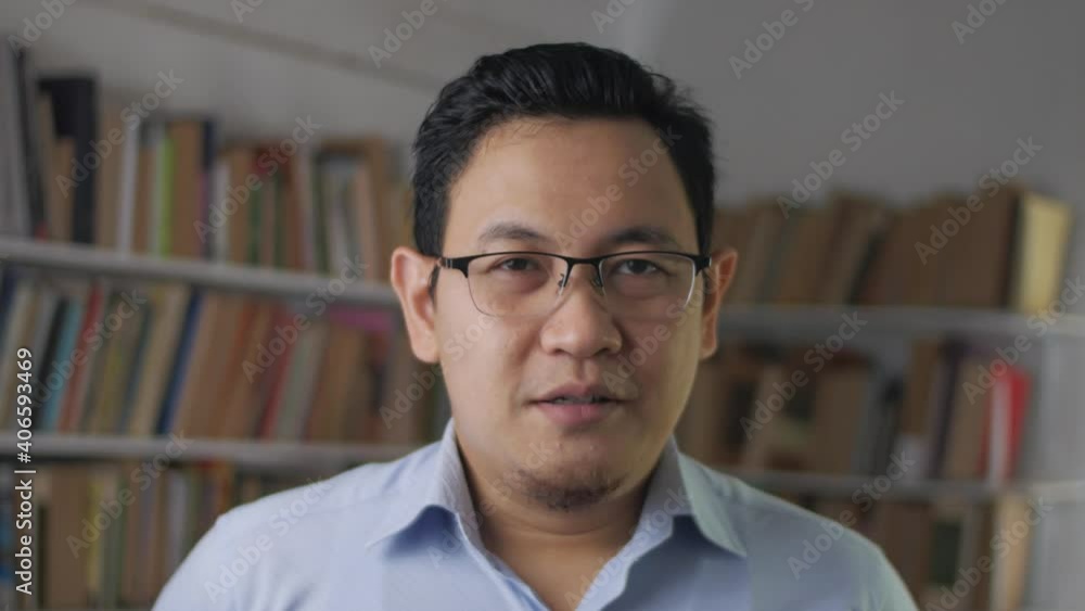 Young Asian man talking to camera while standing inside library, businessman doing video conference