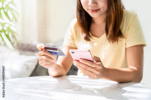 Young asian woman holding a credit card and using smart phone for make an online shopping payment at home