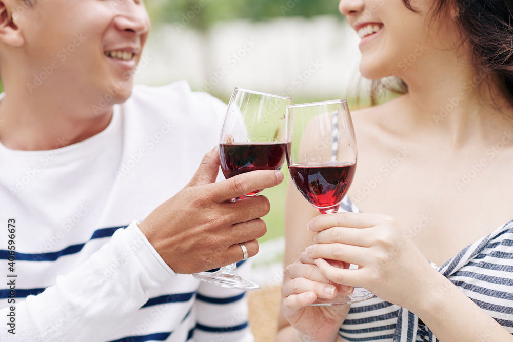 Close-up image of smiling boyfriend and girlfriend drinking red wine when having romantic date outdoors Close-up image of smiling boyfriend and girlfriend drinking red wine when having romantic date outdoors