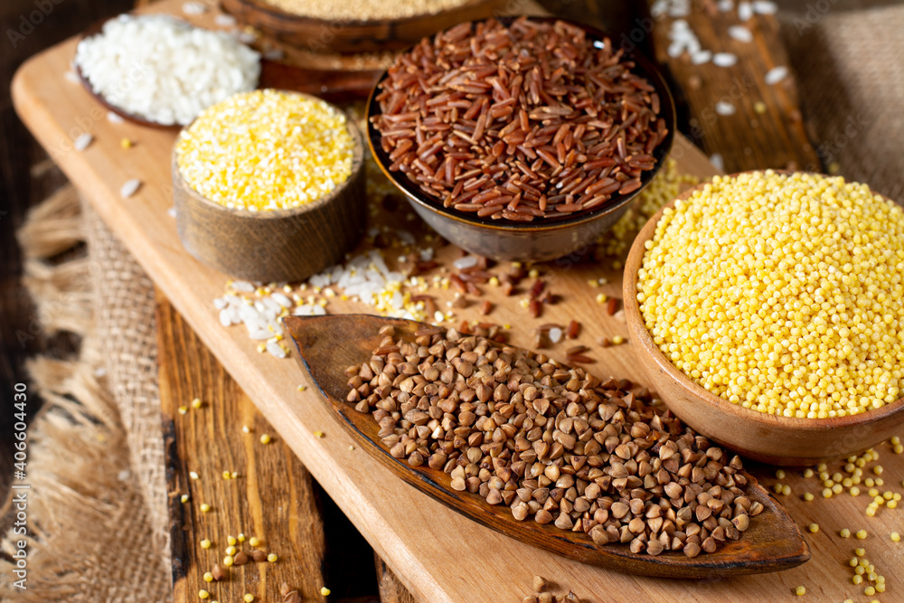 White and red rice, buckwheat, amaranth seeds, corn groats, quinoa and millet in bowls on a brown wooden table. Gluten-free cereals. Closeup White and red rice, buckwheat, amaranth seeds, corn groats, quinoa and millet in bowls on a brown wooden table. Gluten-free cereals. Closeup