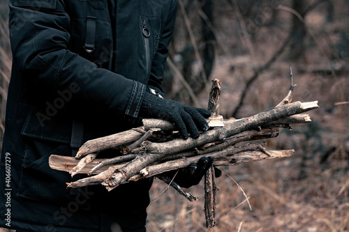 Male hands in black gloves collect firewood for the fire. Bonfire in the autumn forest. Campfire travel trip concept