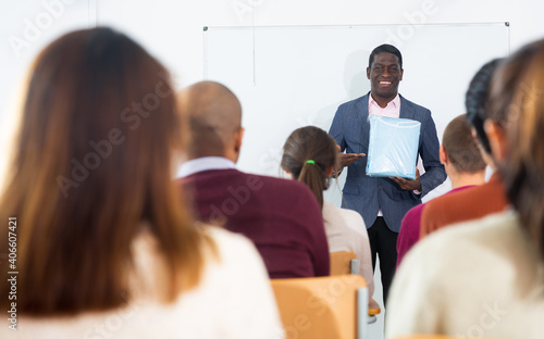 Coach business person teacher delivering lecture speech about product development at conference for group of sitting audience in classroom using whiteboard