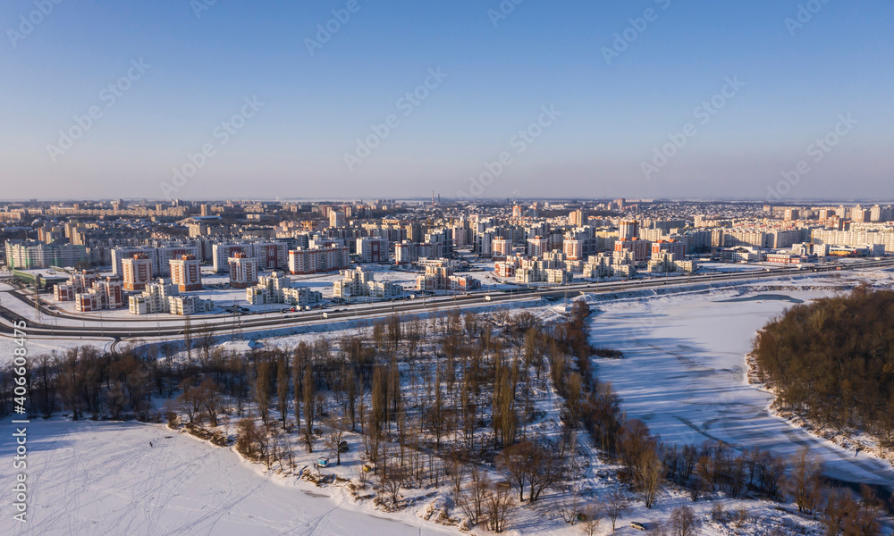 Panorama of the winter city, top view. Frozen river bank, forest, multi-storey buildings. Winter frosty, sunny city from above.