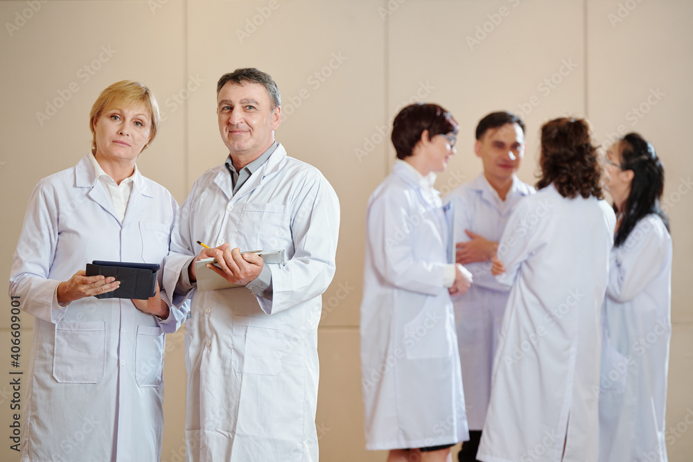Mature scientists with tablet computers standing in hall after having conference with younger colleagues Mature scientists with tablet computers standing in hall after having conference with younger colleagues