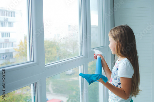 Free Download A little girl sprinkles water from a bottle on the window and wipes it off with a rag. The child helps with cleaning the house. - GFXLoad