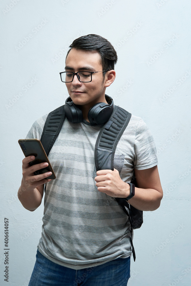 portrait of student, young man looking at cellphone with earphones and backpack on a white background portrait of student, young man looking at cellphone with earphones and backpack on a white background