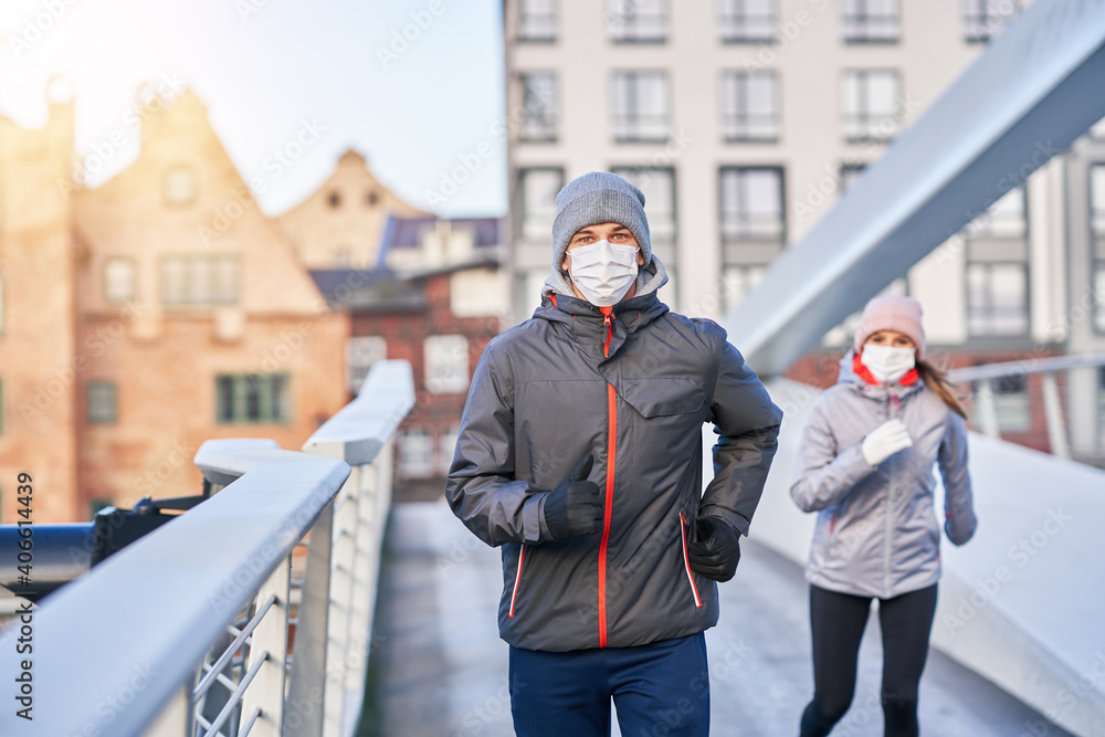 Obraz premium Adult couple jogging in the city in masks during lockdown