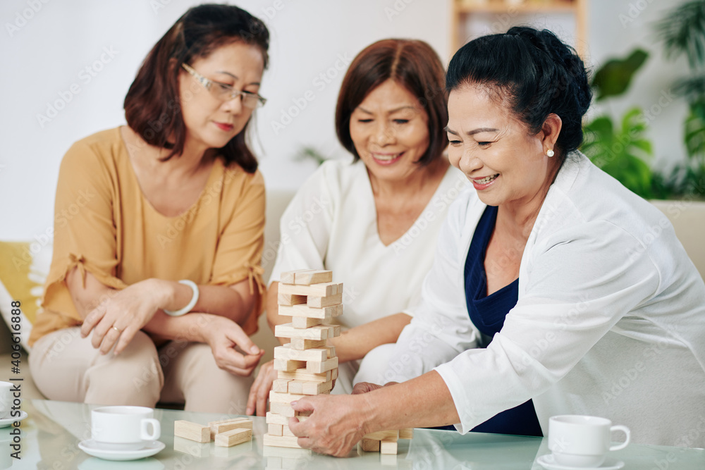 Group of cheerful Asian senior women playing strategy game with blocks of wood and drinking tea Group of cheerful Asian senior women playing strategy game with blocks of wood and drinking tea
