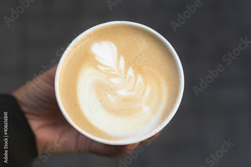 Cappuccino in a paper cup in your hand. Morning delicious coffee to take away. Top view of the foam and a beautiful pattern. Paper disposable cup. Creamy foam, fragrant coffee close-up. Fresh coffee