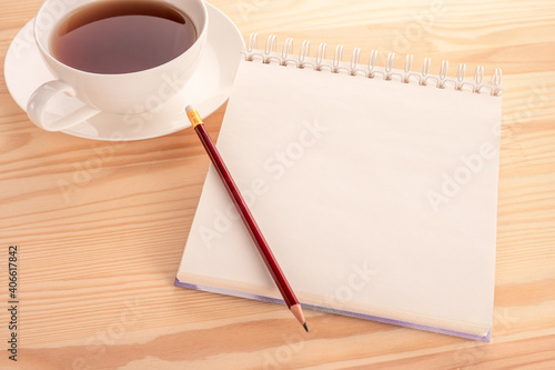 mockup notebook with a blank page on a wooden table and a cup of tea. Open blank page notebook with a copy space and cup of tea