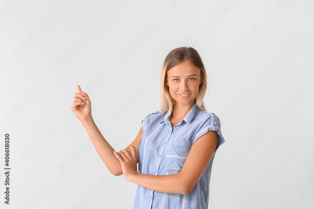 Beautiful young woman pointing at something on light background Beautiful young woman pointing at something on light background