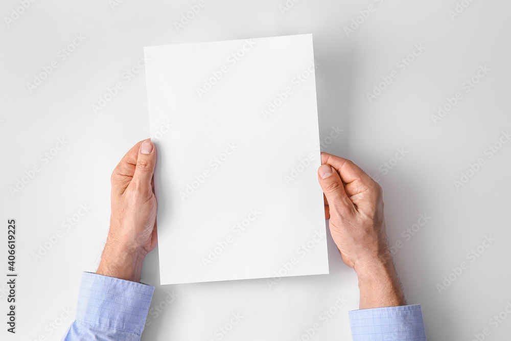 Male hands with blank paper sheet on light background Male hands with blank paper sheet on light background