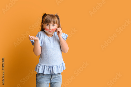 Confused little girl with stylish sunglasses against color background