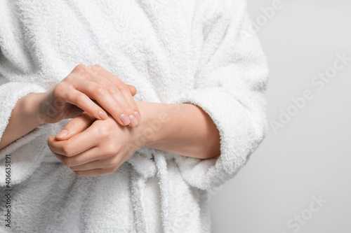 A woman in a robe moisturizes her hands with a nourishing cream.