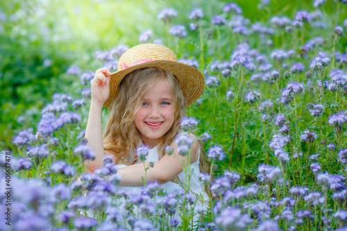 little girl in a straw hat in a purple field in summer