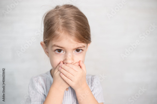 portrait of little girl, child closing his mouth with hands. Speech therapist, speech problems, stammering, mumbling.