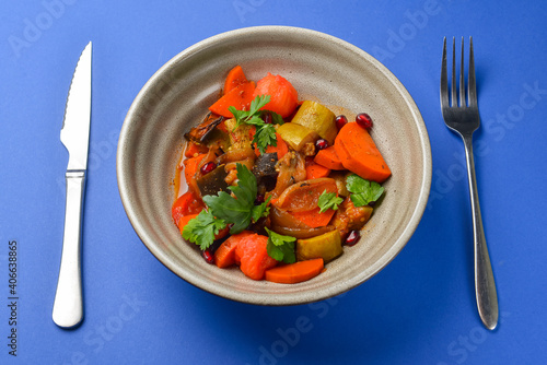 Baked vegetable salad in a cermaic bowl over blue background. Delicious healthy autumn or winter salad.