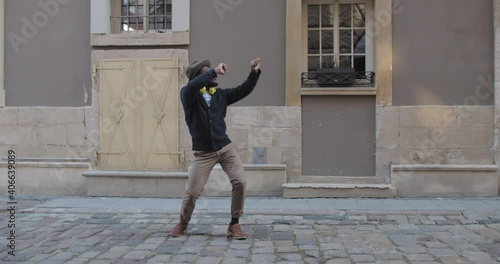 Handsome afro american man in hat with headphones dancing while standing at old city street. Cheerful guy in stylish clothes moving in rhytm.Concept of fun. Outdoors photo