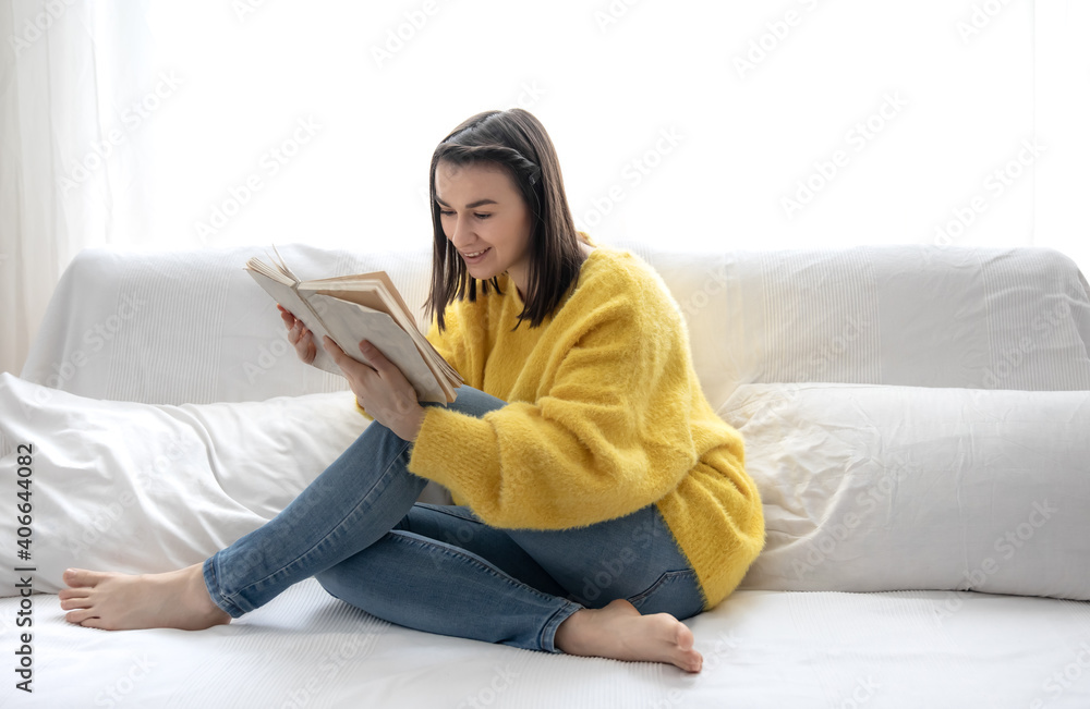 A cute girl in a yellow sweater is reading a book at home on the couch. A cute girl in a yellow sweater is reading a book at home on the couch.