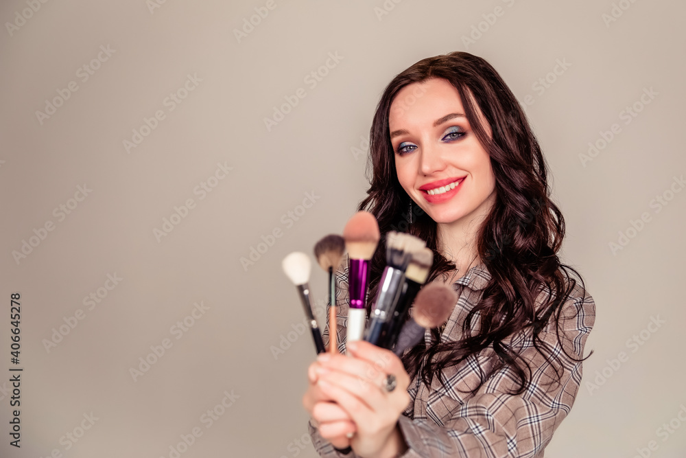 Young beautiful woman holding makeup brushes in her hands and posing on grey background at studio. Young beautiful woman holding makeup brushes in her hands and posing on grey background at studio.